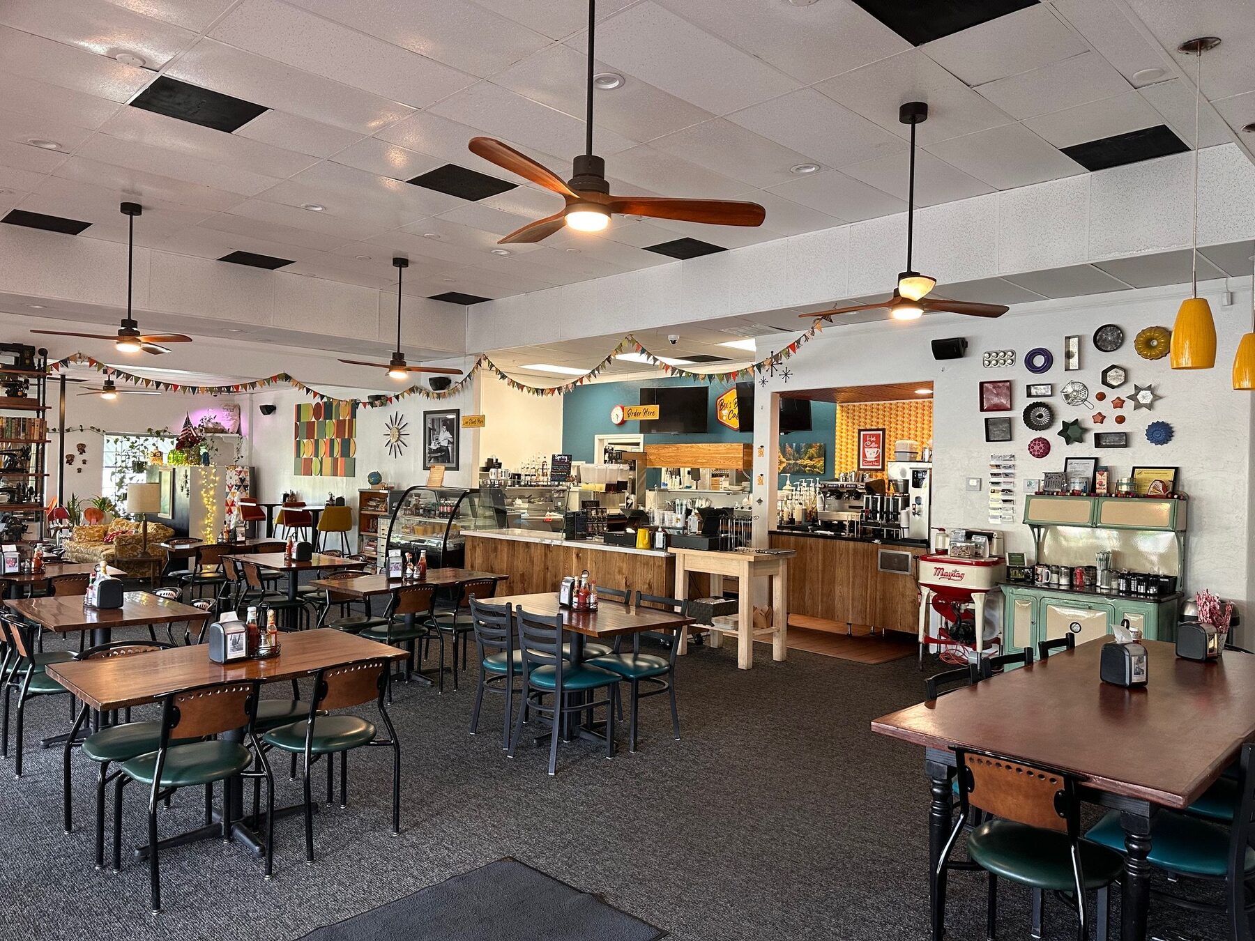 Retro mid-century dining room at Bee's Bakery Cafe with wood tables, teal walls and string lighting