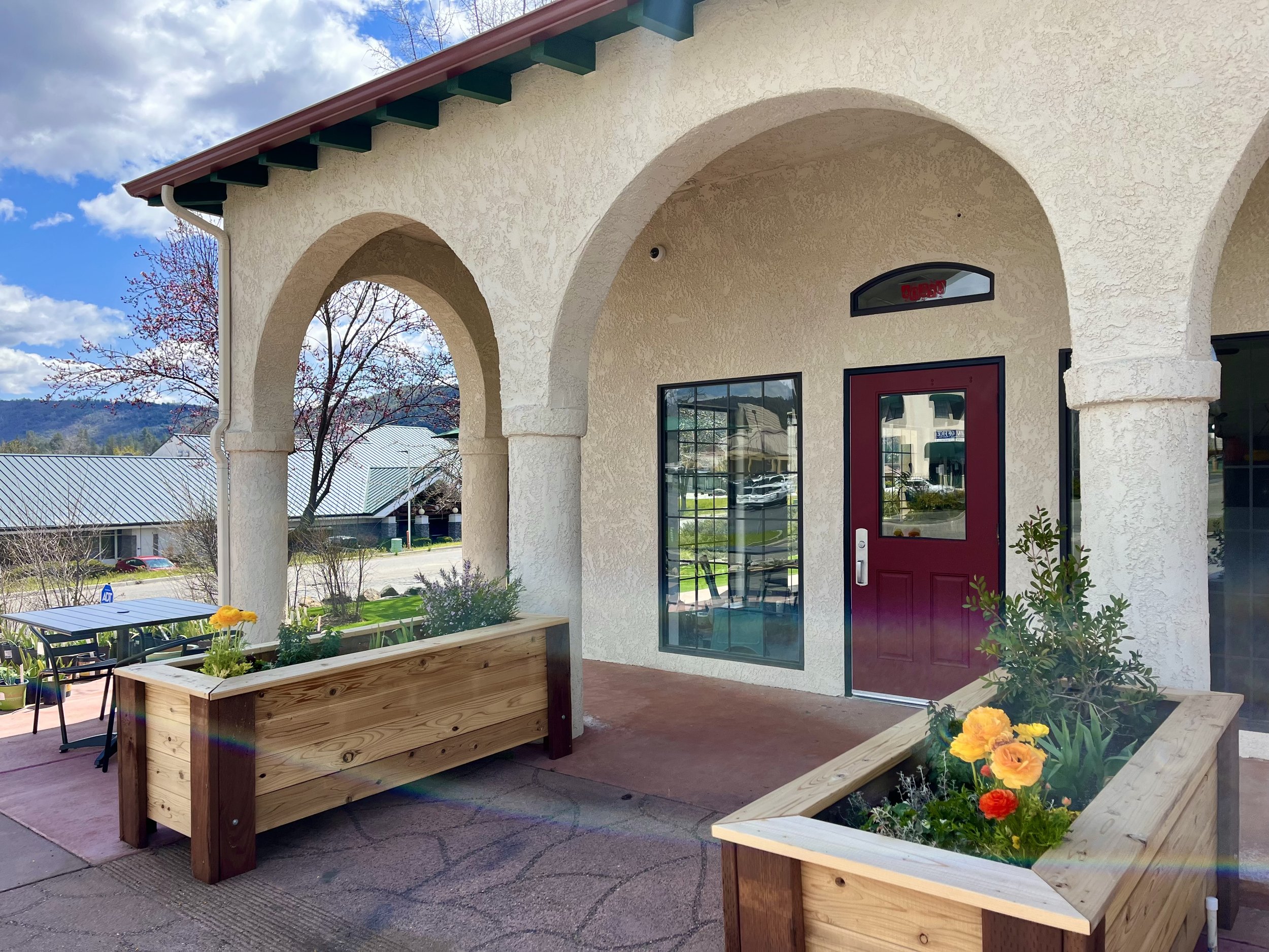 The exterior entrance of Bee's Bakery Cafe, featuring stucco arches and large planter boxes.