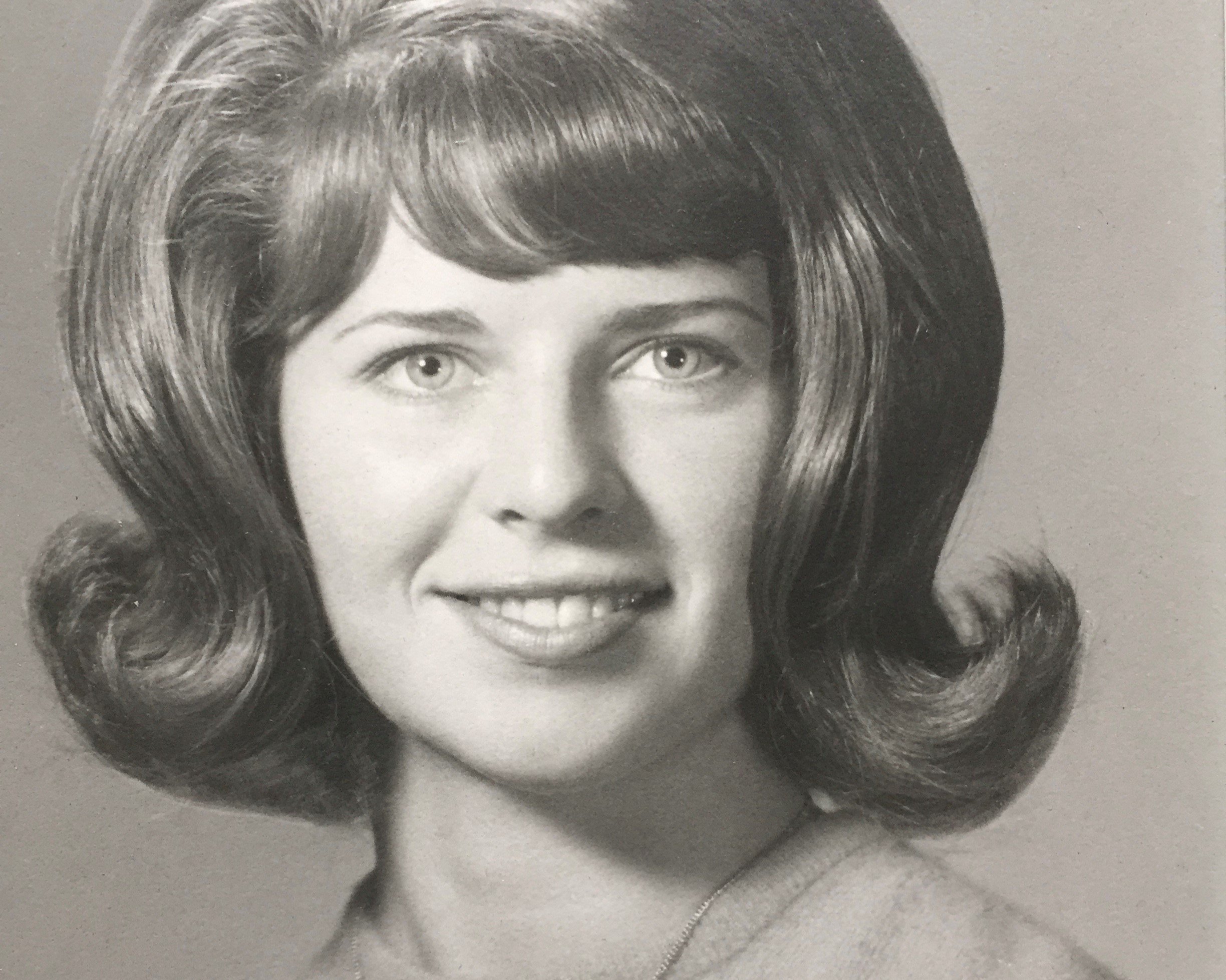 Vintage black-and-white portrait of a smiling young woman with a 1960s bouffant hairstyle.