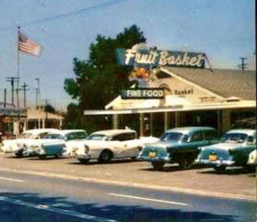 Vintage color photograph of a roadside business called 'Fruit Basket' with several classic 1950s cars parked in front.