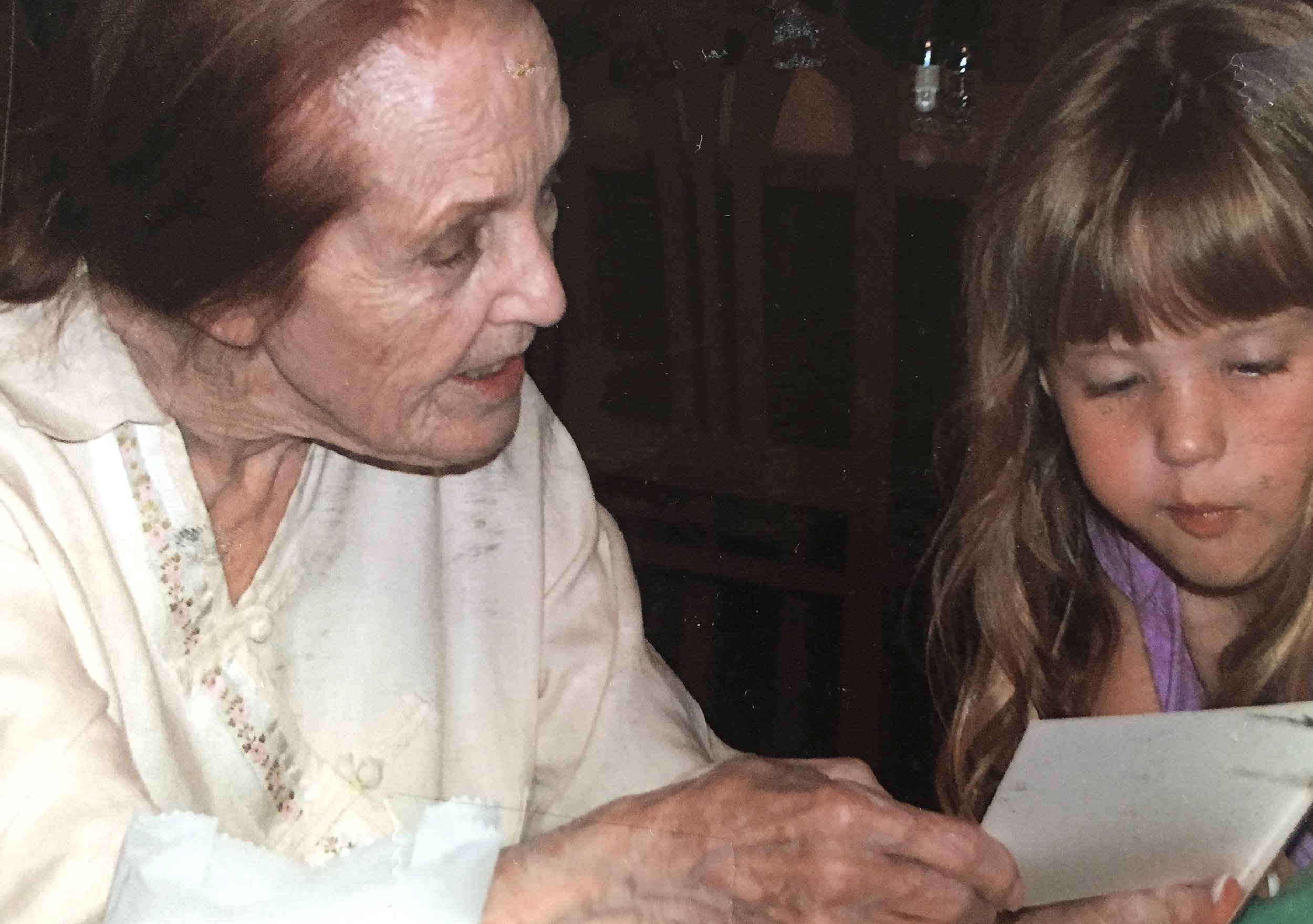 An older woman and a young girl looking closely at a small white card or paper together.