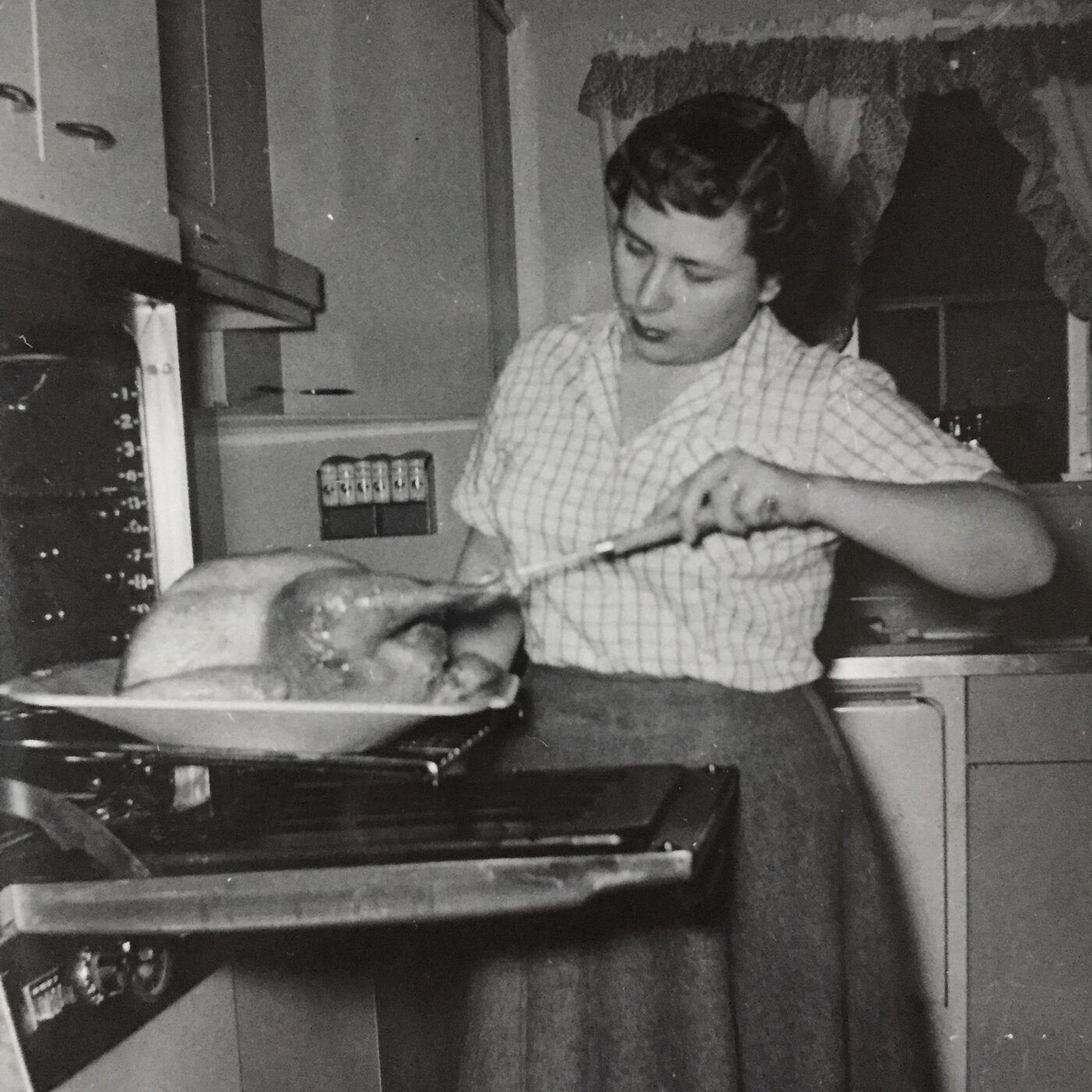 Vintage black-and-white photograph of a woman preparing a holiday turkey in a mid-century kitchen